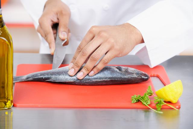 A portrait of a biracial chef preparing fish in a commercial kitchen.