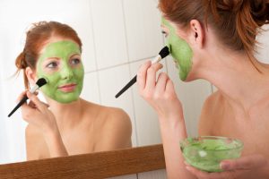 woman-putting-on-green-face-mask-home