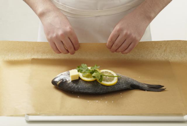 Wrapping whole sea bream in baking paper, with lemons, herb, and butter